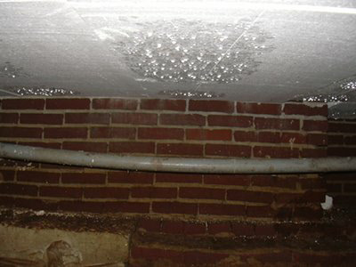 Doorhangende pvc-leiding langs een bakstenen muur in de kruipruimte